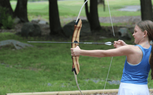 A younger girl doing archery outside
